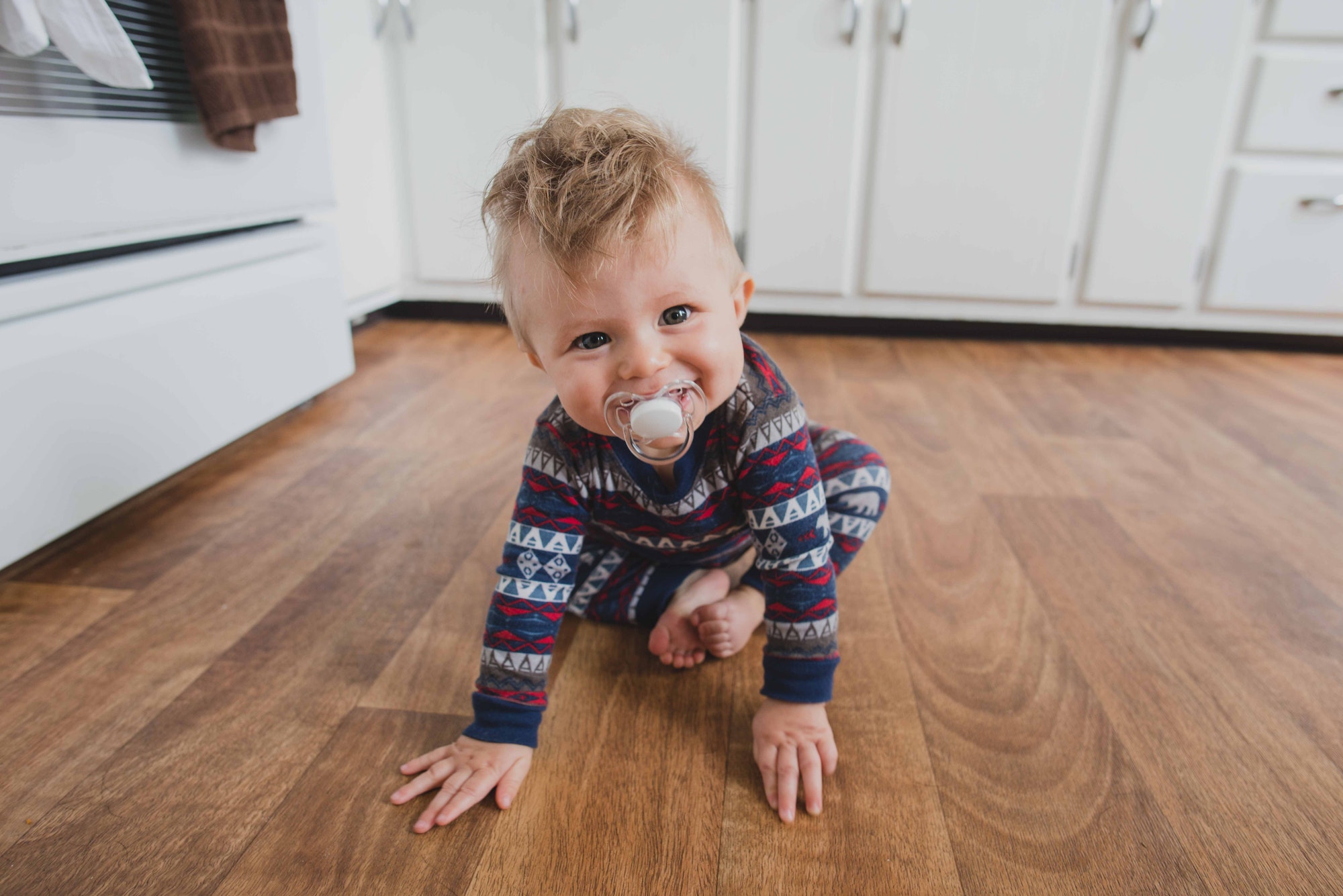 lifestyle picture of a cute, happy baby boy with pacifier learning how to crawl at home